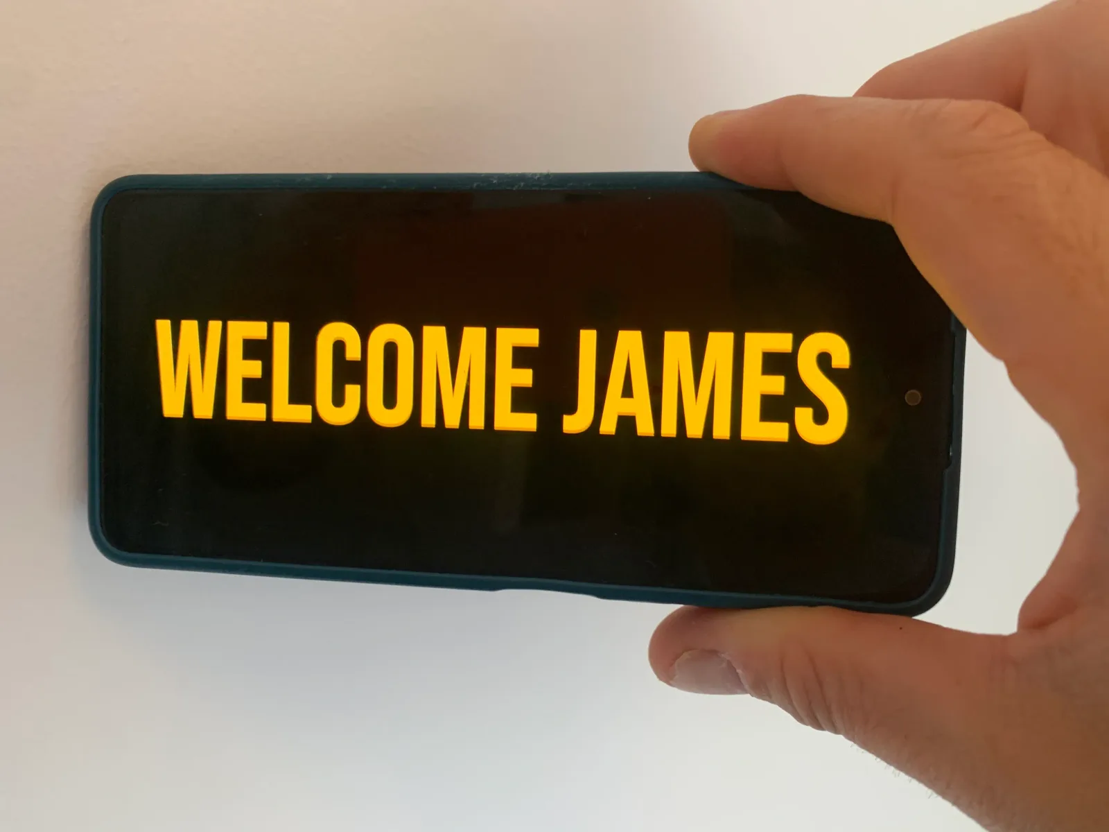 Real phone displaying a large Welcome James airport pickup message in landscape orientation